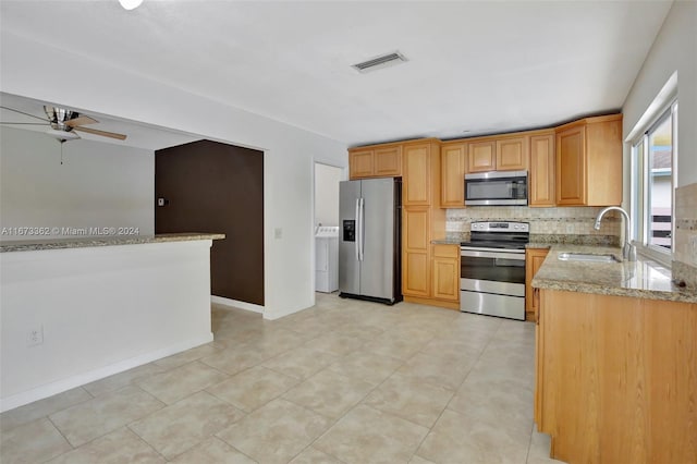 kitchen featuring appliances with stainless steel finishes, washer / clothes dryer, tasteful backsplash, light stone countertops, and sink