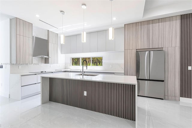 kitchen with pendant lighting, stainless steel fridge, sink, a center island with sink, and wall chimney range hood