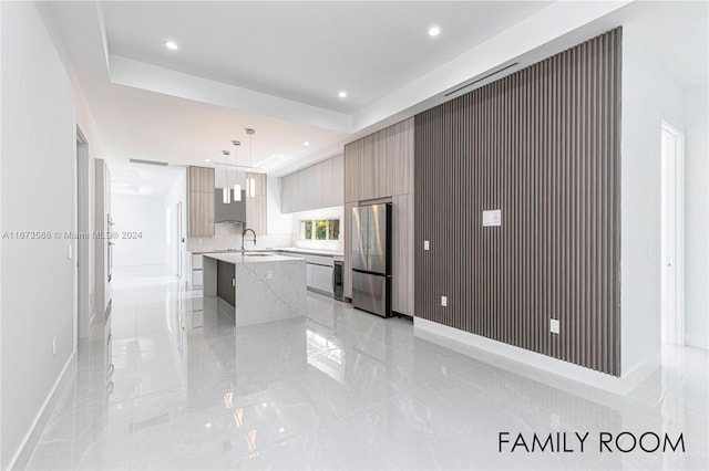 kitchen with hanging light fixtures, sink, a center island with sink, stainless steel refrigerator, and a breakfast bar