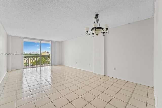 tiled spare room with an inviting chandelier, a textured ceiling, and a wall of windows