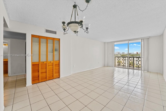 spare room featuring expansive windows, light tile patterned floors, a textured ceiling, and a chandelier