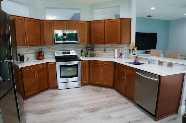 kitchen featuring kitchen peninsula, sink, tasteful backsplash, appliances with stainless steel finishes, and light wood-type flooring