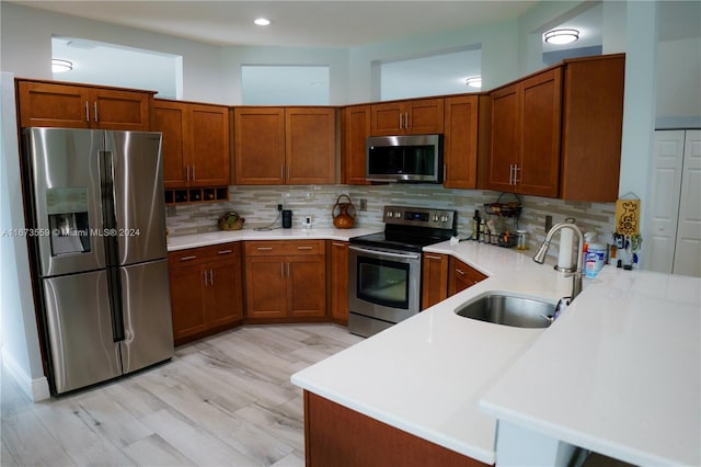 kitchen with sink, kitchen peninsula, backsplash, stainless steel appliances, and light wood-type flooring