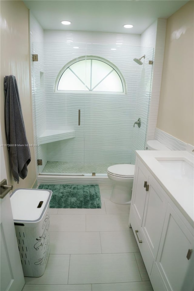 bathroom with tile patterned flooring, a shower with door, vanity, and toilet