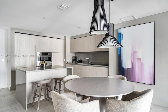 kitchen with sink, a kitchen island, double oven, light brown cabinetry, and light wood-type flooring