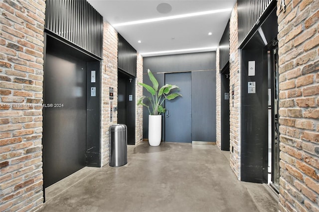 hallway featuring elevator, brick wall, and concrete floors