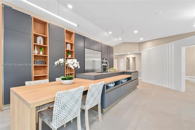 kitchen with built in fridge, lofted ceiling, a kitchen island with sink, and a kitchen breakfast bar