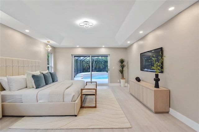 bedroom featuring a tray ceiling, light wood-type flooring, and access to outside