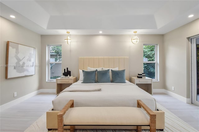 bedroom with a raised ceiling, multiple windows, and light hardwood / wood-style flooring