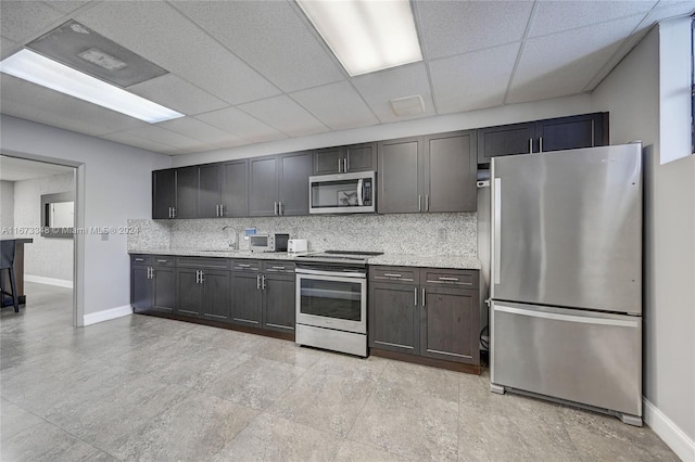 kitchen featuring sink, a drop ceiling, backsplash, stainless steel appliances, and light stone counters