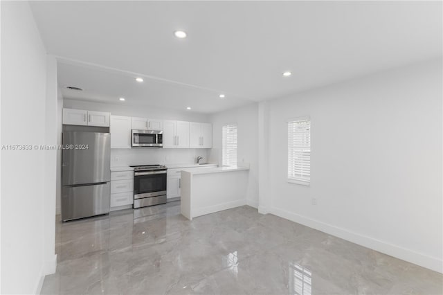 kitchen with appliances with stainless steel finishes, kitchen peninsula, white cabinets, and sink