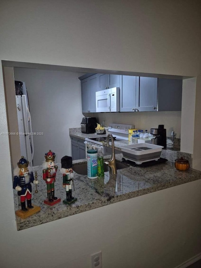 kitchen with light stone counters, white appliances, and sink