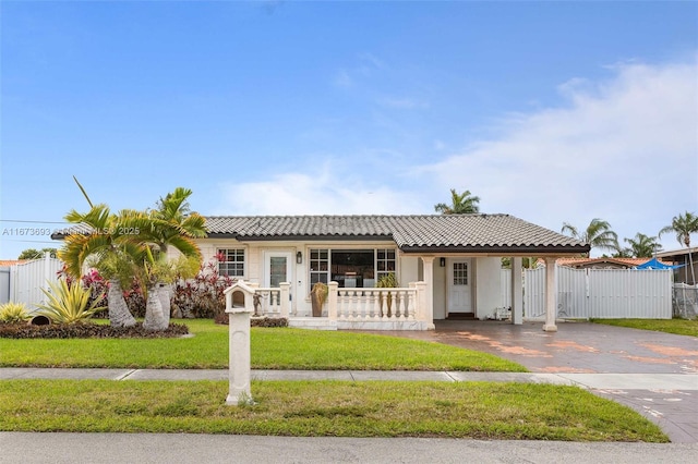 view of front of property featuring aphalt driveway, covered porch, a tile roof, fence, and a front lawn