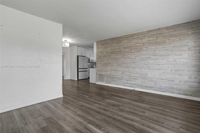 unfurnished living room featuring baseboards, a textured ceiling, visible vents, and dark wood-type flooring