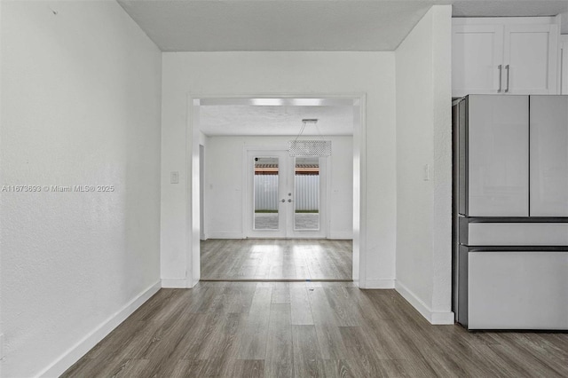 hall featuring a textured ceiling, french doors, wood finished floors, and baseboards