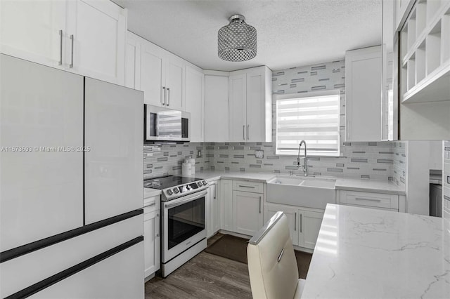 kitchen with light stone counters, stainless steel microwave, white cabinets, a sink, and range with electric cooktop