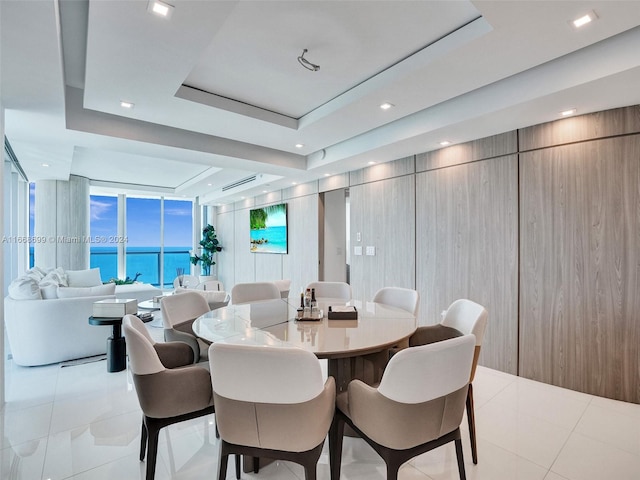 dining area with a water view, light tile patterned floors, and a raised ceiling