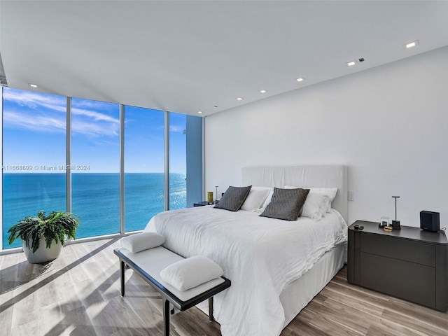 bedroom featuring a water view, expansive windows, light hardwood / wood-style floors, and access to exterior