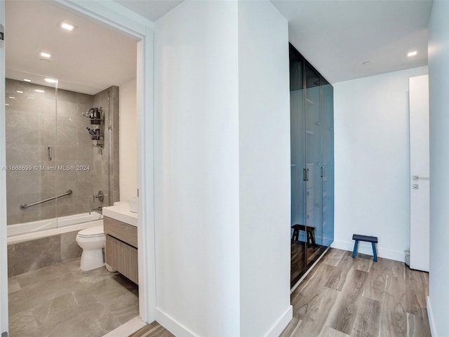 full bathroom with hardwood / wood-style flooring, shower / bath combination with glass door, toilet, and vanity