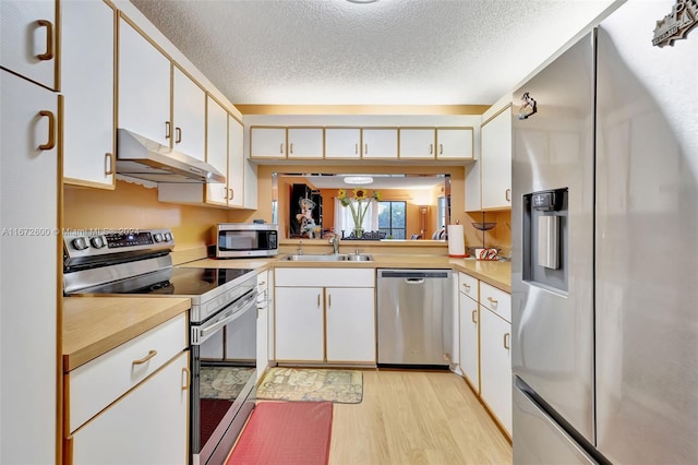 kitchen with sink, light wood-type flooring, white cabinetry, appliances with stainless steel finishes, and a textured ceiling