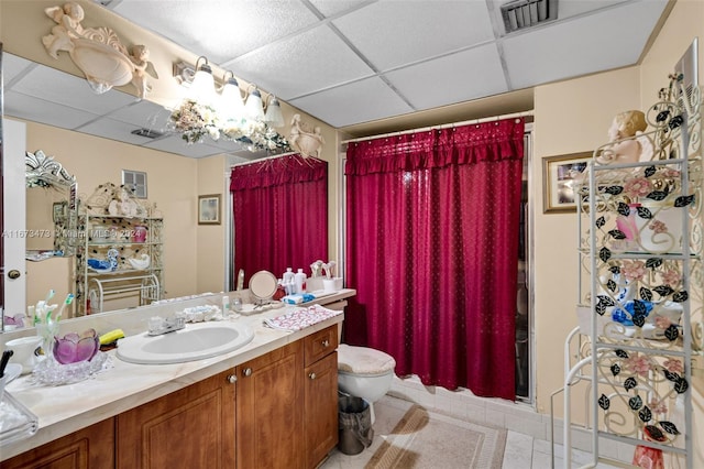 bathroom with walk in shower, a drop ceiling, vanity, tile patterned floors, and toilet