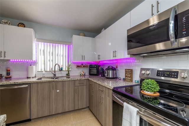 kitchen with light stone counters, white cabinets, stainless steel appliances, and sink