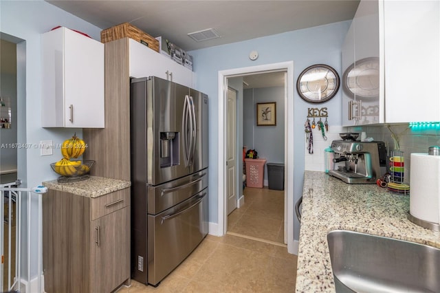 kitchen featuring white cabinets, light tile patterned flooring, stainless steel fridge, light stone countertops, and decorative backsplash