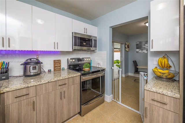 kitchen featuring light stone counters, white cabinets, stainless steel appliances, and decorative backsplash