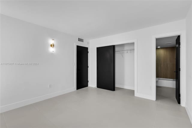 unfurnished bedroom with ensuite bath, a closet, and light tile patterned flooring