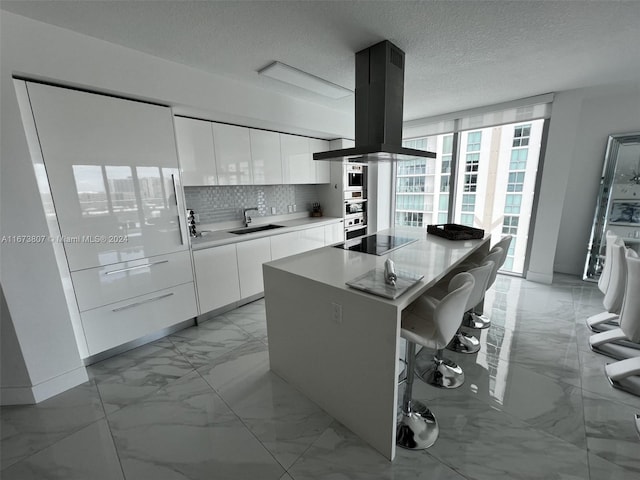 kitchen with white cabinets, a kitchen island, island exhaust hood, backsplash, and a breakfast bar