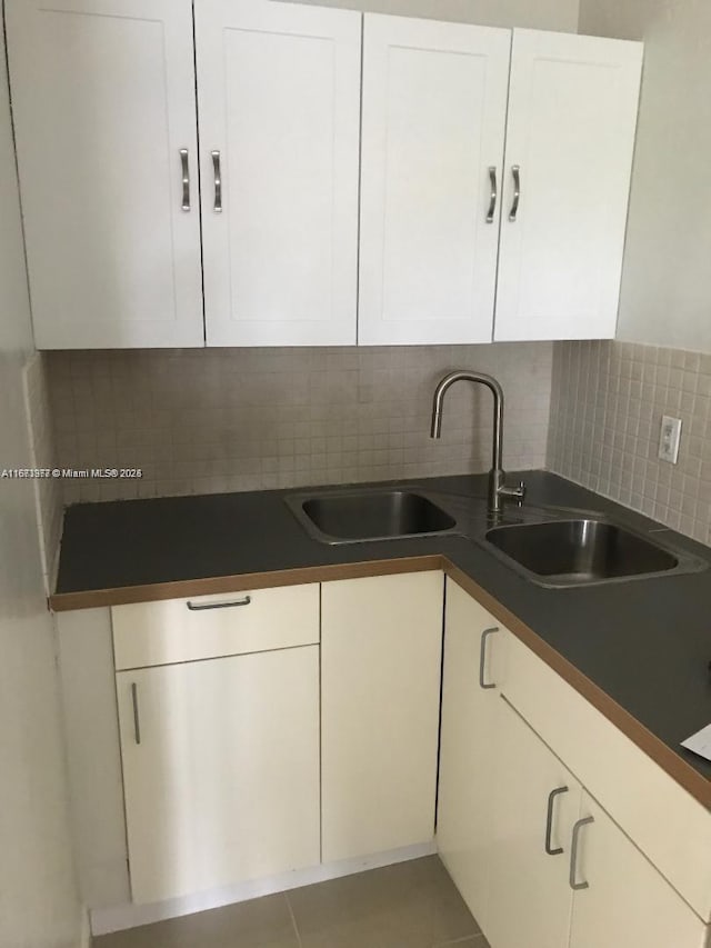 kitchen featuring decorative backsplash, dark countertops, a sink, and white cabinets