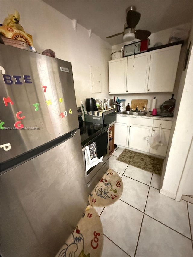 kitchen with dark countertops, appliances with stainless steel finishes, white cabinets, a sink, and light tile patterned flooring