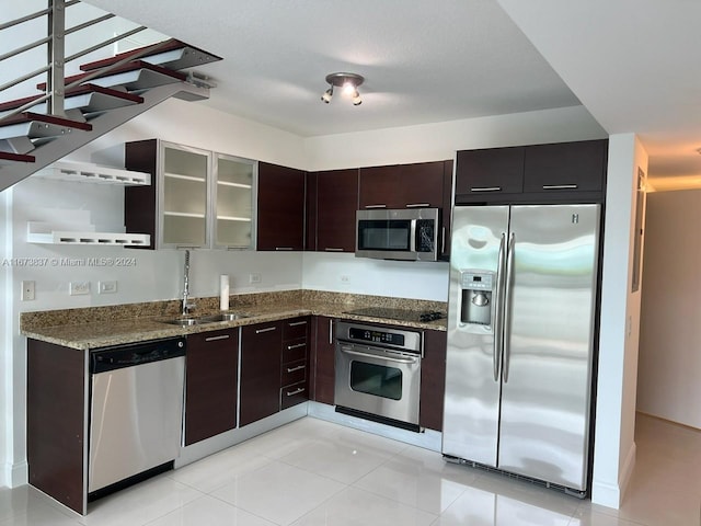 kitchen featuring stainless steel appliances, sink, light stone countertops, dark brown cabinetry, and light tile patterned floors