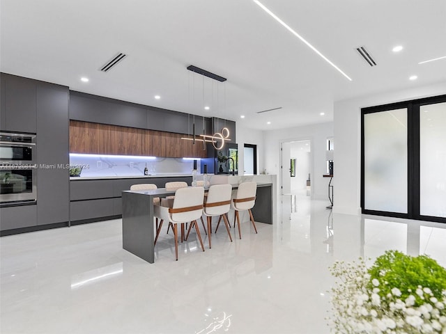 kitchen featuring pendant lighting, stainless steel double oven, a kitchen island, and a kitchen bar