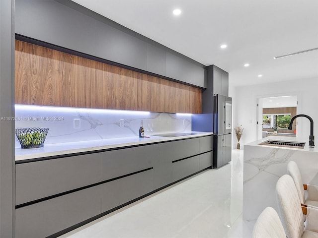 kitchen with light stone countertops, sink, tasteful backsplash, and black electric stovetop