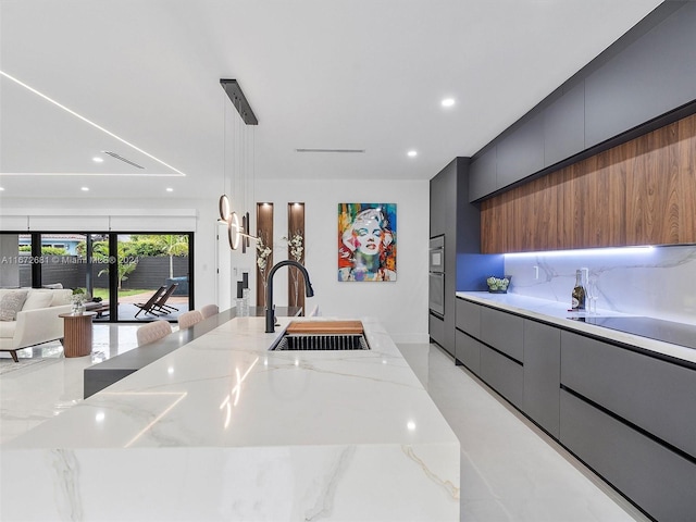 kitchen featuring light stone counters, sink, decorative light fixtures, oven, and a spacious island