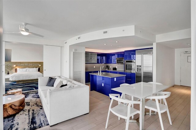 interior space with ceiling fan, a center island with sink, light hardwood / wood-style flooring, blue cabinetry, and appliances with stainless steel finishes