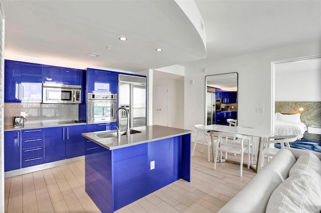 kitchen featuring a kitchen island with sink, tasteful backsplash, sink, light hardwood / wood-style flooring, and appliances with stainless steel finishes