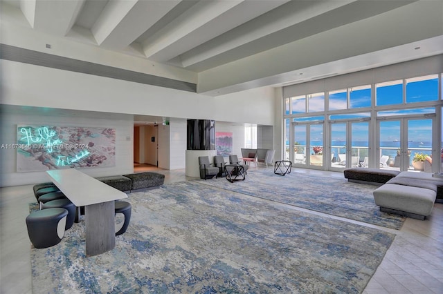 living room featuring a water view, beamed ceiling, hardwood / wood-style floors, a towering ceiling, and french doors