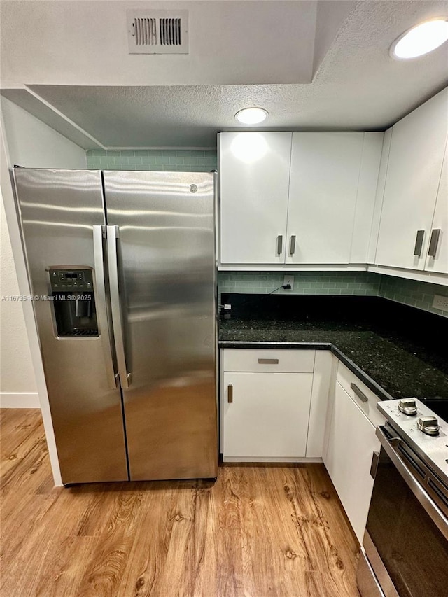 kitchen featuring appliances with stainless steel finishes, light wood-type flooring, white cabinets, dark stone counters, and a textured ceiling