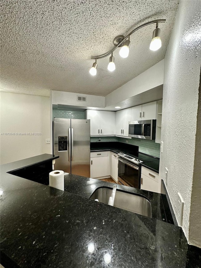 kitchen with stainless steel appliances, white cabinets, a textured ceiling, and dark stone counters