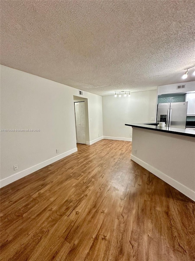 unfurnished living room featuring track lighting, wood-type flooring, and a textured ceiling