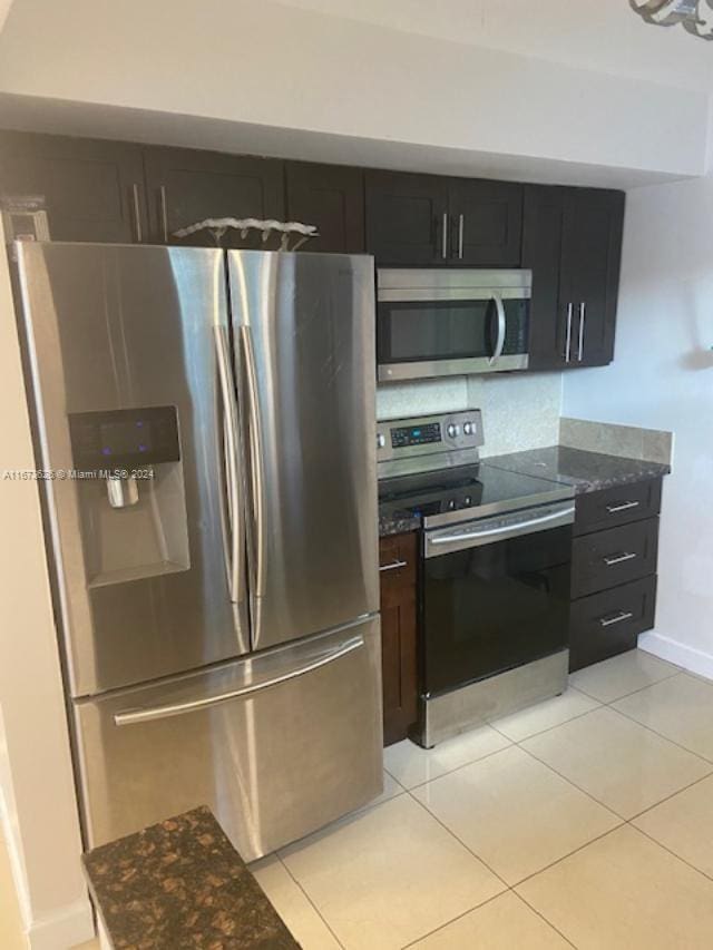 kitchen with decorative backsplash, appliances with stainless steel finishes, light tile patterned floors, and dark stone counters