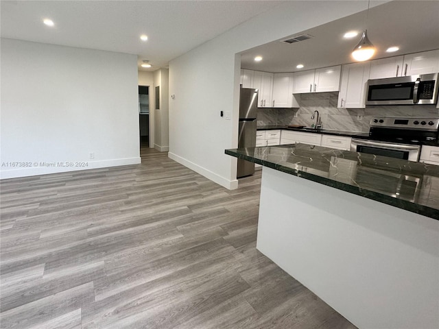 kitchen with white cabinets, hanging light fixtures, light hardwood / wood-style flooring, appliances with stainless steel finishes, and dark stone countertops