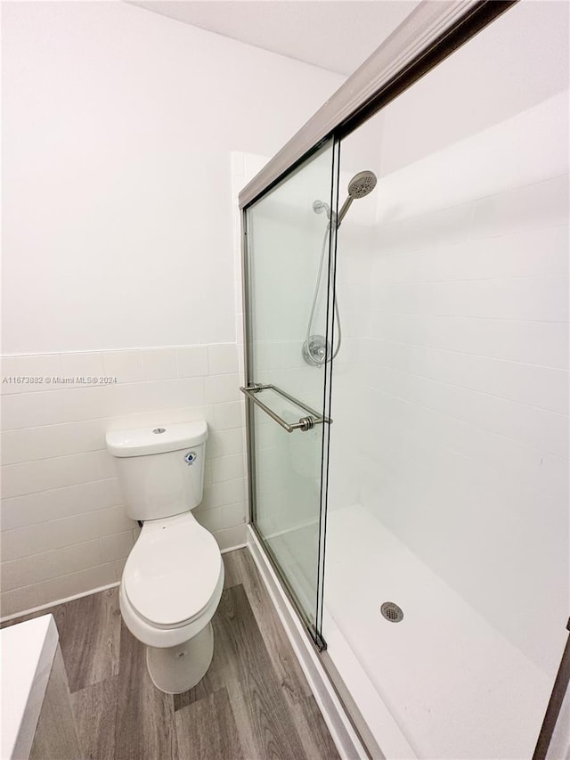 bathroom featuring tile walls, hardwood / wood-style floors, toilet, and a shower with door