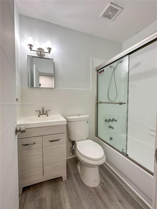 full bathroom featuring vanity, hardwood / wood-style floors, bath / shower combo with glass door, tile walls, and toilet