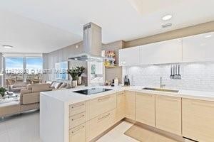 kitchen with black electric cooktop, sink, kitchen peninsula, island range hood, and light brown cabinetry