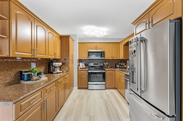 kitchen featuring light wood-type flooring, tasteful backsplash, appliances with stainless steel finishes, stone counters, and a textured ceiling