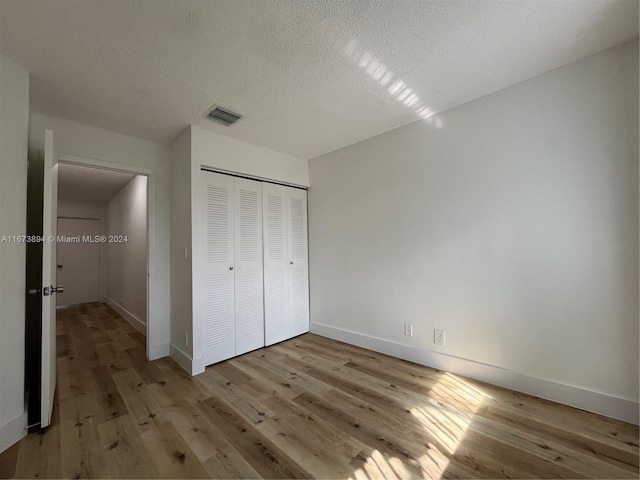 unfurnished bedroom featuring a closet, a textured ceiling, and light wood-type flooring