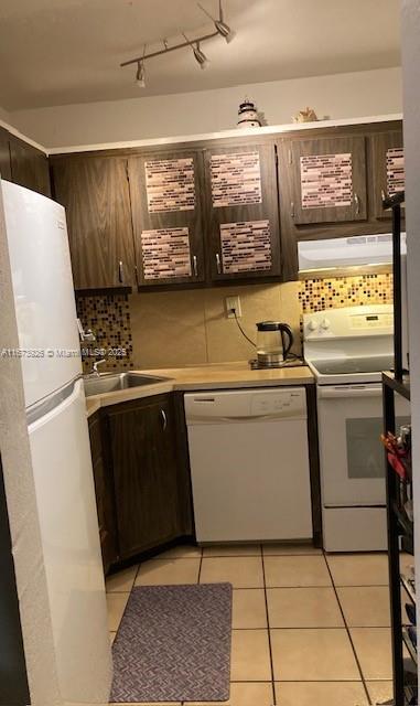 kitchen featuring light tile patterned flooring, under cabinet range hood, white appliances, light countertops, and decorative backsplash